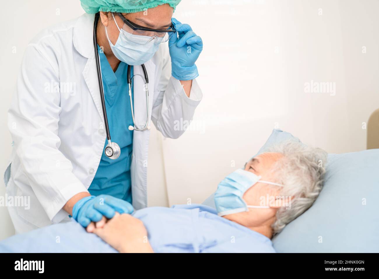 Ein Arzt hilft der älteren oder älteren asiatischen Patientin, die eine Gesichtsmaske trägt, im Krankenhaus, um eine Sicherheitsinfektion zu schützen und das Covid-19 Coronavirus zu töten. Stockfoto