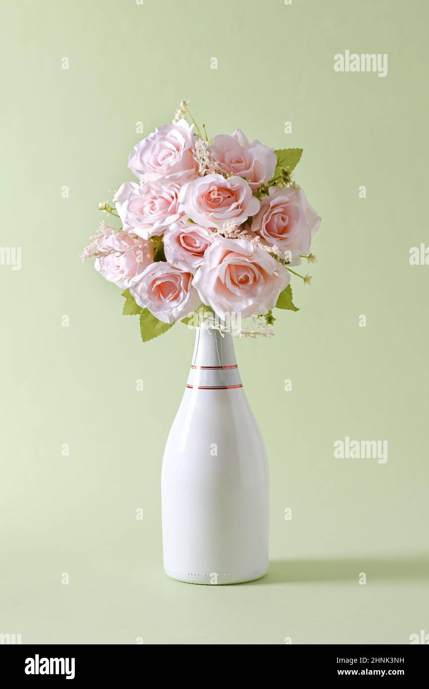 Bouquet von frischen rosa Blumen in einer stilvollen unbeschrifteten weißen Champagnerflasche über Grün mit Kopierplatz für Valentinstag Stockfoto