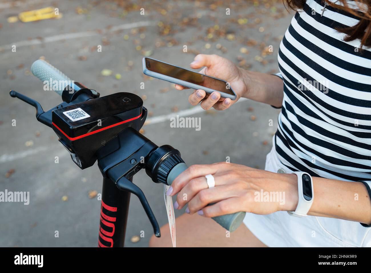 Ein Mädchen mietet einen Elektroroller mit einer Anwendung auf ihrem Telefon. Selbstbedienungs-Elektroroller-Verleih auf der Straße. Stockfoto