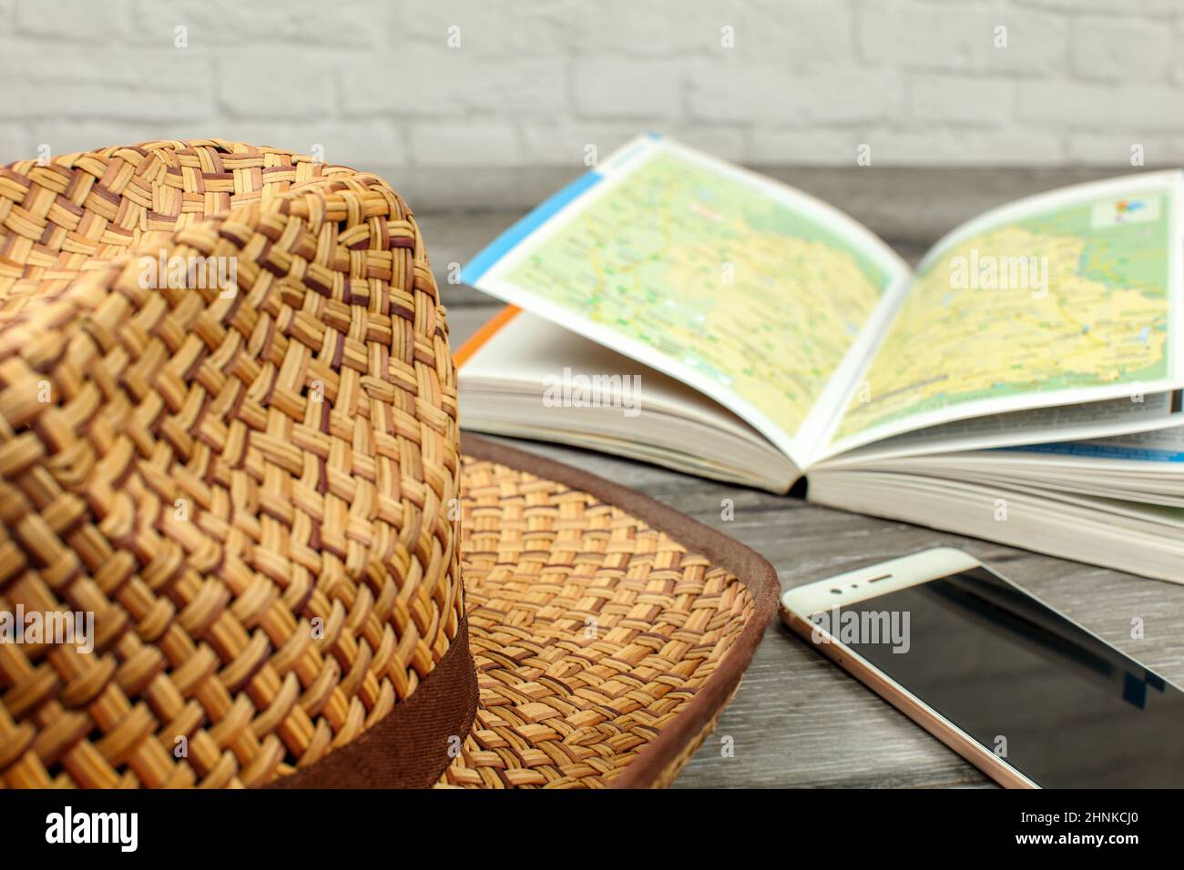 Strohhut, Reiseführer mit Karte und Mobiltelefon auf grau Holzschreibtisch. Reiseplanung Konzept. Stockfoto