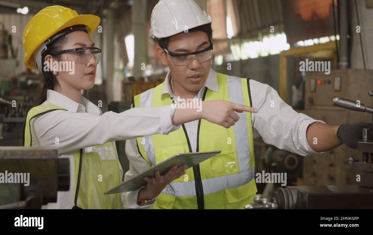 Maschinenbauingenieurin Frau und Mann mit uniformiertem Hardhut und Schutzbrille, die an einer Metalldrehmaschine in der Werkstatt arbeiten Stockfoto
