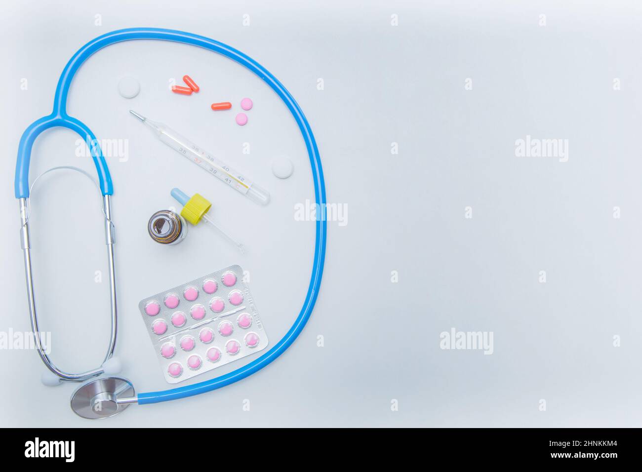 Das Stethoskop liegt auf einem weißen Hintergrund in einem Kreis, darin befindet sich ein Thermometer, Medikamente und Tropfen aus einer laufenden Nase. Stockfoto