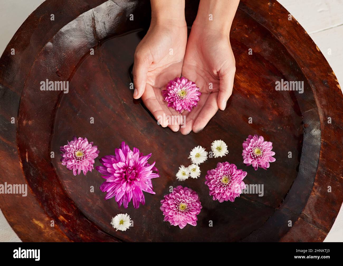 Entspannen Sie sich im Spa. Ein kurzer Schuss einer Frau reicht in einer mit Blumen gefüllten Wasserschale in einem Spa. Stockfoto