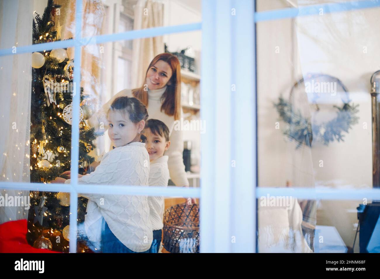 Süße kleine Kinder helfen Eltern, Weihnachtsbaum zu Hause schmücken, glückliche Eltern und kleine Kinder, die sich auf Weihnachten und Neujahr vorbereiten, schmücken hous Stockfoto