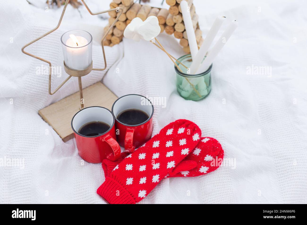Weihnachtlicher Hintergrund, rote Fäustlinge, Tassen Kaffee auf dem Schnee, Sternenkerze. Picknick im Freien. Frohe Weihnachten. Stockfoto