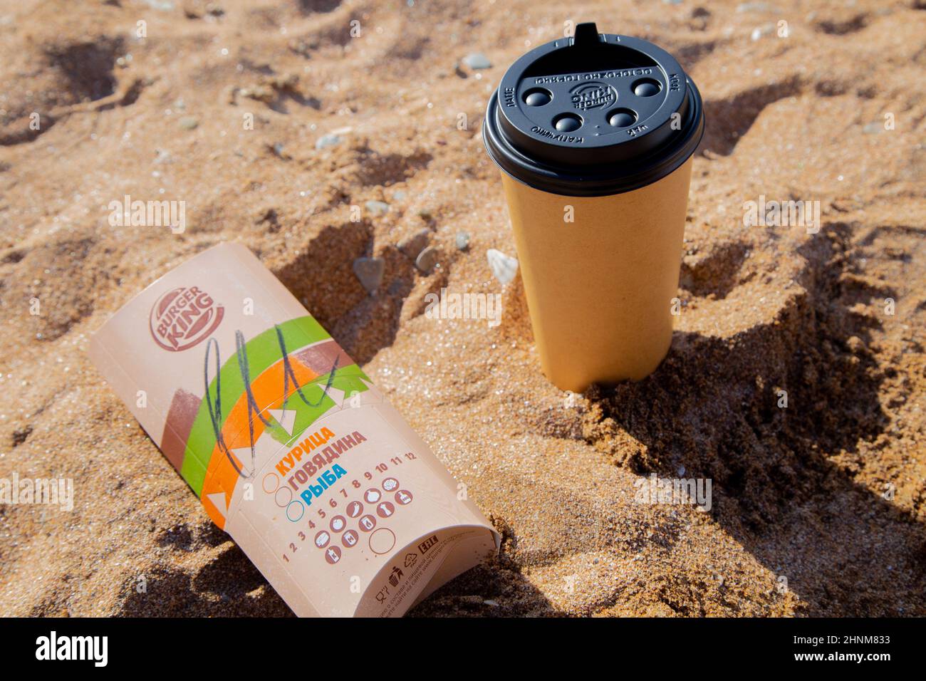 Kaffee in einer Einweg-Tasse und Burger von Burger King liegen auf dem Sand unter der Sonne Stockfoto