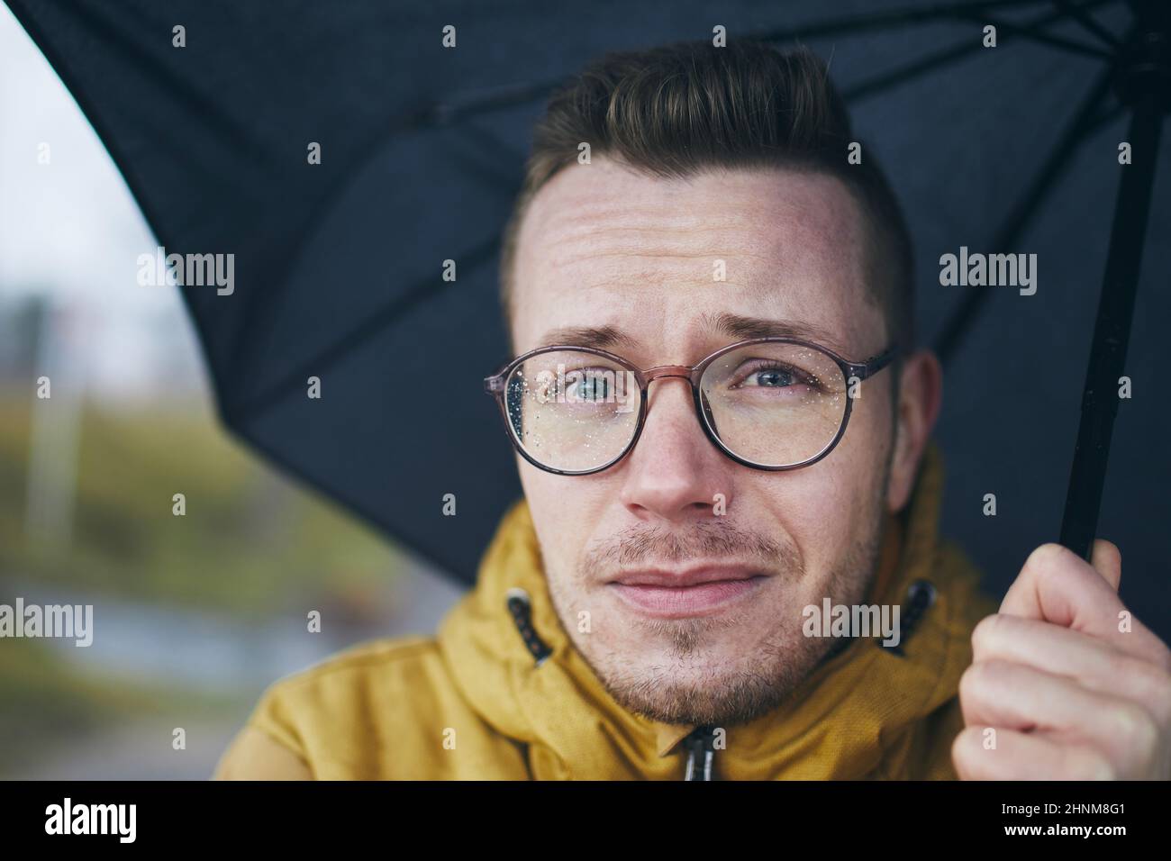 Porträt eines jungen Mannes mit Brille unter Regenschirm im Regen. Themen Wetter eine Meteorologie. Stockfoto