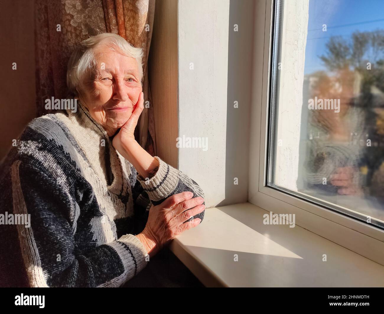 Alte, einsame Frau sitzt am Fenster in seinem Haus. Stockfoto