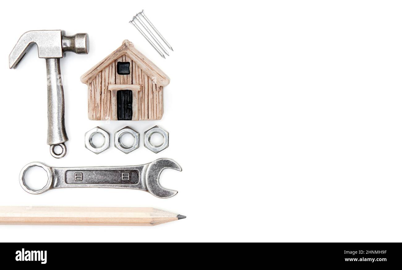 Miniatur-Spielzeughaus, kleiner Hammer, Schraubenschlüssel, Nüsse, Nägel und ein Bleistift isoliert auf weißem Hintergrund. Home Verbesserung und Reparatur-Konzept. Stockfoto