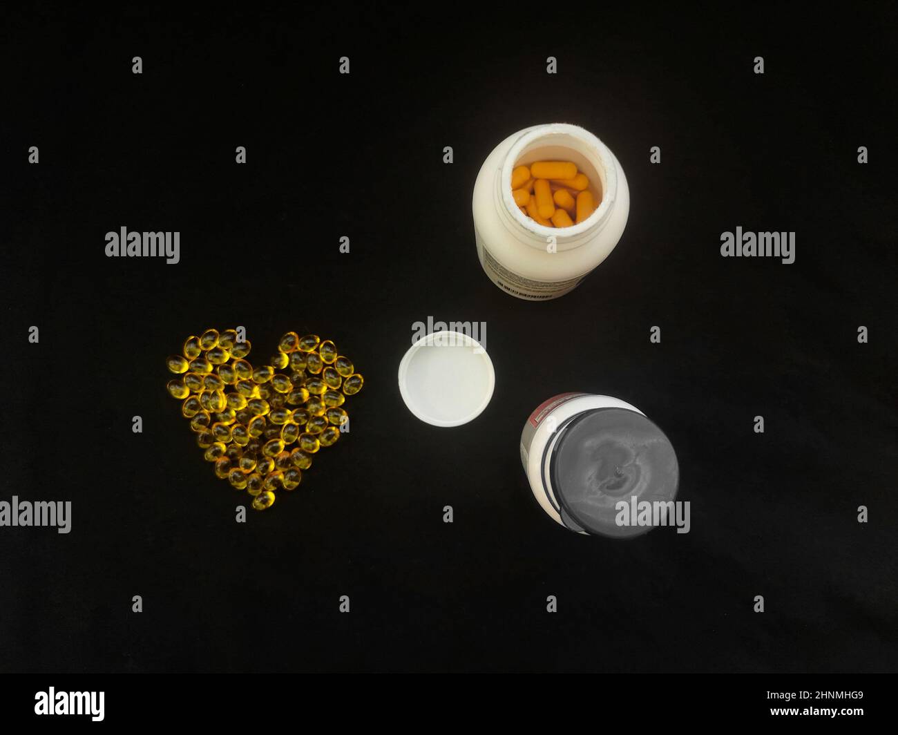 Gelbe transparente herzförmige Kapseln und Gläser mit Pillen auf schwarzem Hintergrund Stockfoto