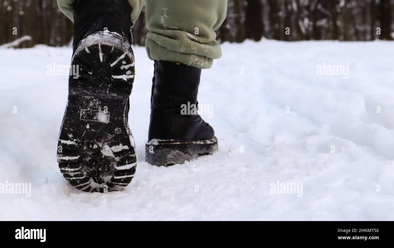 Weibliche Beine in schwarzen Stiefeln, Winterspaziergang im Schnee. Aktive Frau, die im Winterwald von der Kamera wegläuft. Konzentriere dich auf deine Beine. Schönes weißes Winterwetter mit frischem Schneefall. Stockfoto