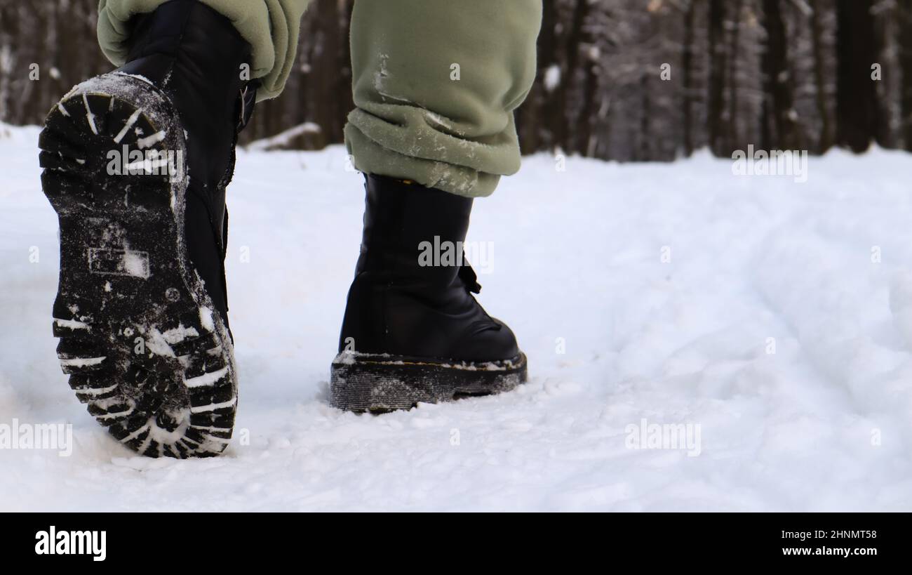 Weibliche Beine in schwarzen Stiefeln, Winterspaziergang im Schnee. Aktive Frau, die im Winterwald von der Kamera wegläuft. Konzentriere dich auf deine Beine. Schönes weißes Winterwetter mit frischem Schneefall. Stockfoto