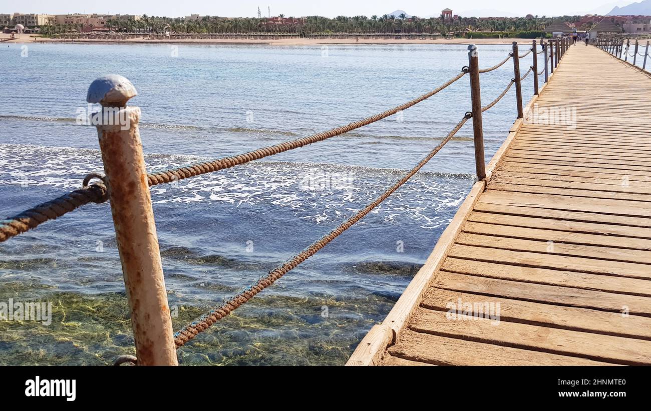 Langer Ponton am Roten Meer in Ägypten. Ponton für den Abstieg ins Wasser. Holzbrücke auf dem Gelände des Amway Hotels in Sharm El Sheikh mit Metallzäunen und einem Seil über dem Meer mit Wellen Stockfoto