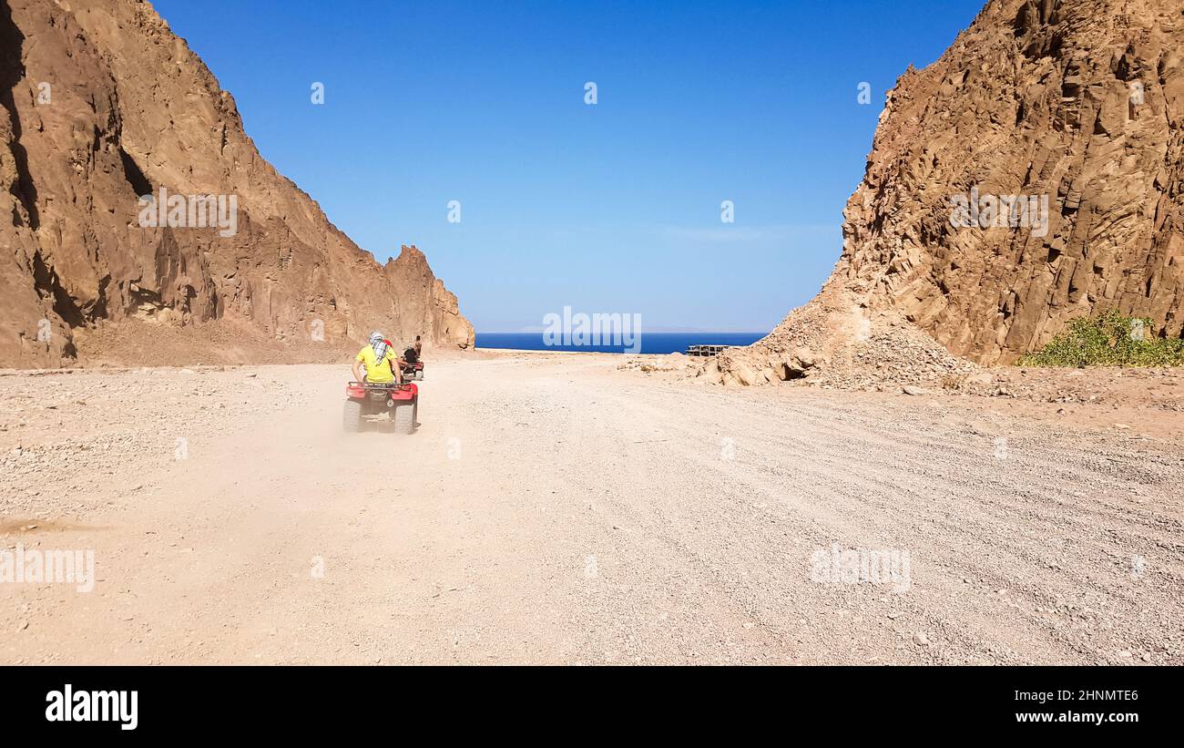 Wüste in Ägypten. Felsige Sandhügel. Ein einsame Tourist auf einem ATV in der Wüste vor dem Hintergrund des blauen Himmels und der Berge läuft in Richtung des Roten Meeres. Landschaft in der Wüste. Stockfoto