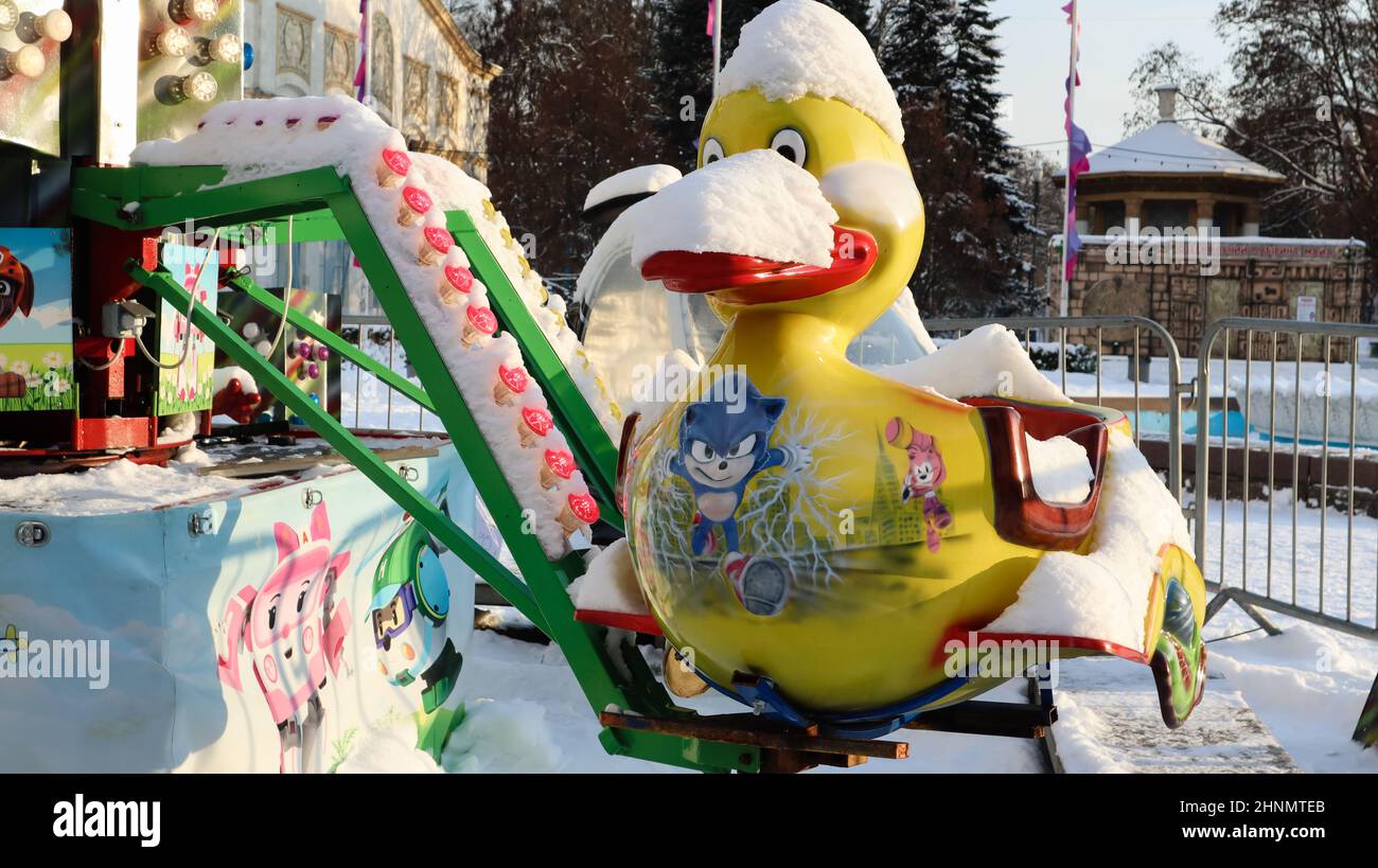 Das leere Karussell ist mit Schnee bedeckt. Nahaufnahme des schneebedeckten bunten Entenkarussells beim lustigen Jahrmarkt-Karneval während des Wintertags. Stockfoto