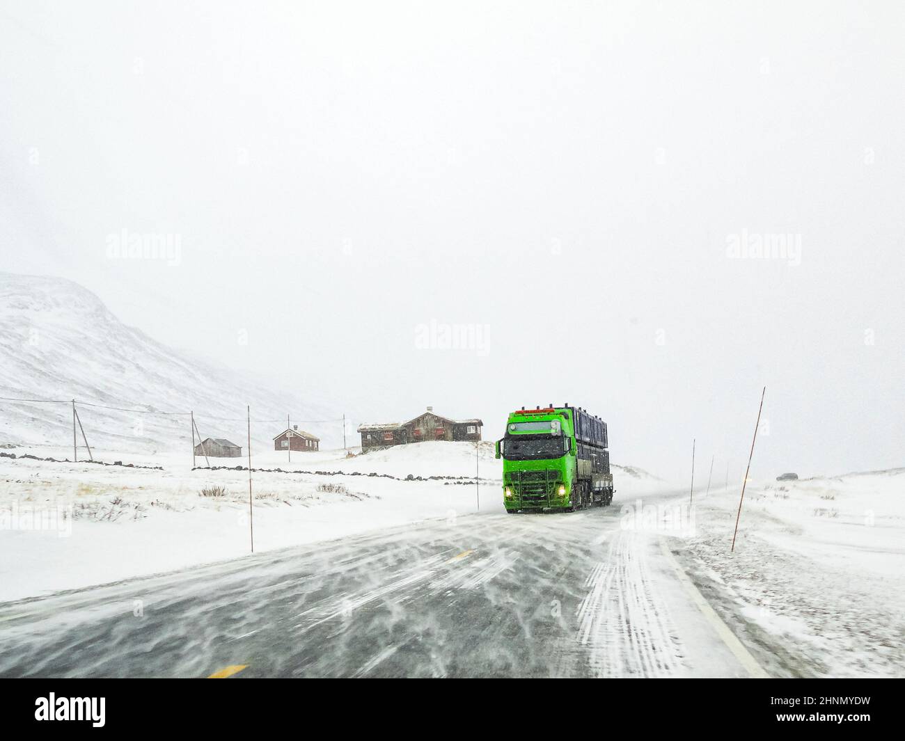Fahrt durch verschneite Straßenlandschaft, Norwegen. Grüner LKW vorne. Stockfoto