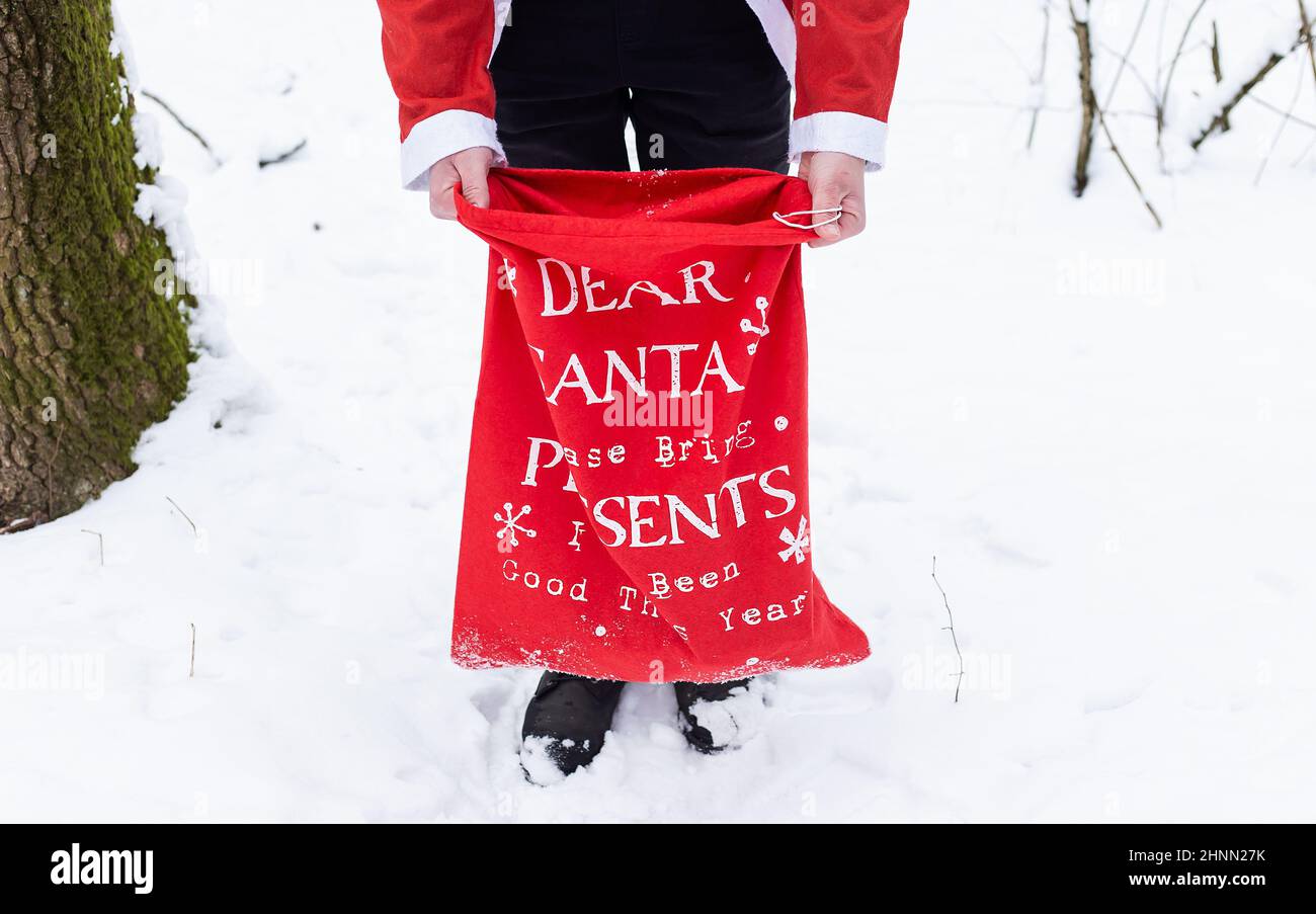 Ein Mann, der als Weihnachtsmann gekleidet ist, hält eine große rote Tasche mit Geschenken für Kinder in der Hand. Stockfoto