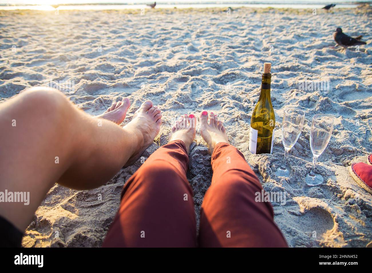 Fröhliches, stilvolles Paar Beine beim Sonnenbaden am Strand, Wein trinken Stockfoto