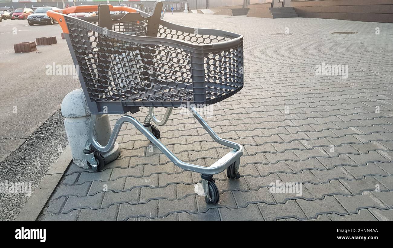 Leerer Lebensmittelkarren im Freien in der Nähe des Supermarkts. Einsamkeit, Karren-Isolation, Quarantäne, Coronavirus. Ein leerer Plastikkorb auf Rädern mit gelben Kunststoffteilen auf dem Bürgersteig in der Nähe des Ladens. Stockfoto