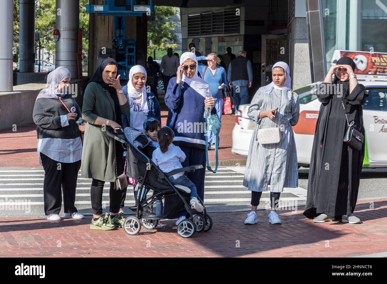 arabisch aussehende Frauen in traditioneller Kleidung mit Kopftuch, die an einer Fußgängerüberführung eine Straße überqueren Stockfoto