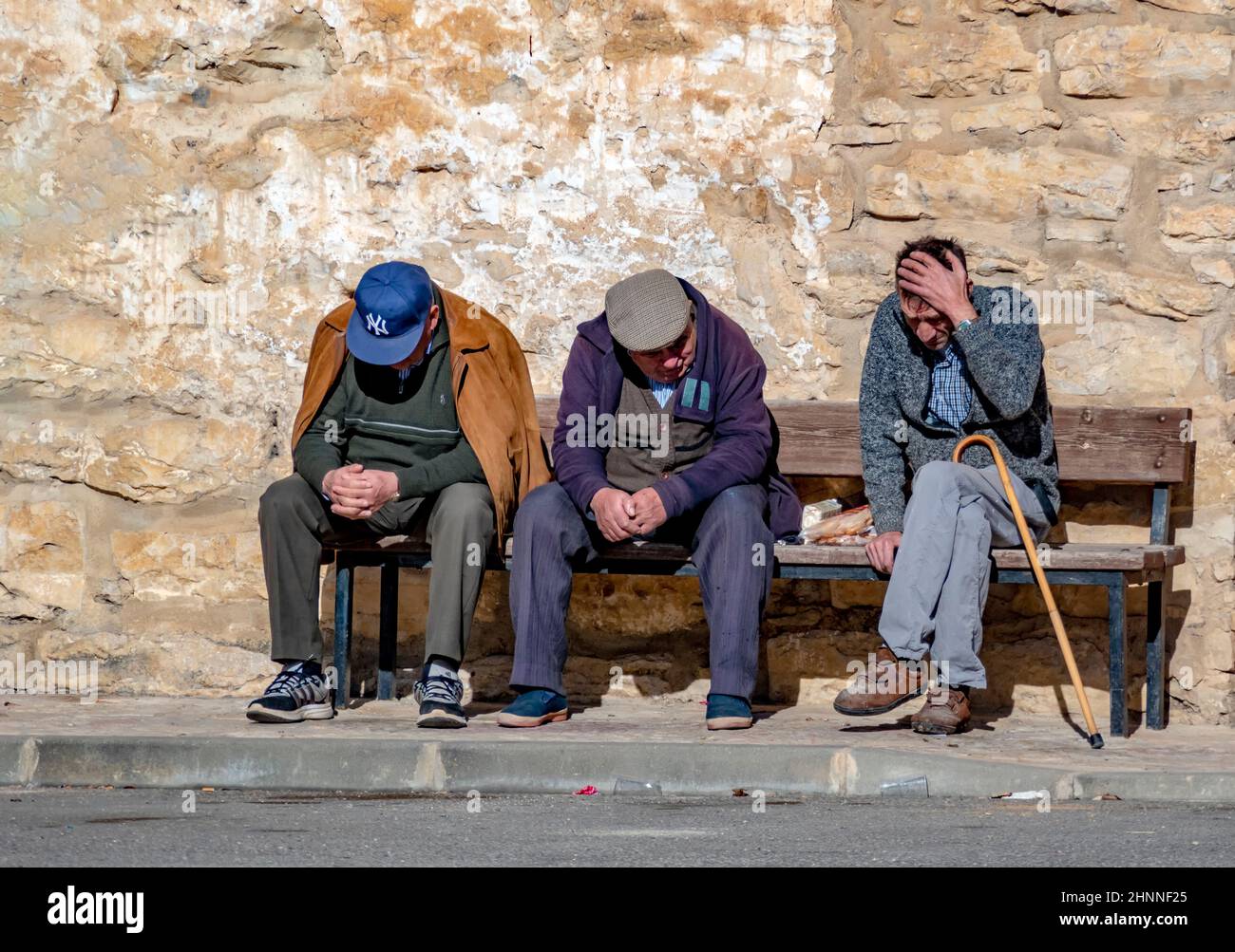 Drei ältere Männer sitzen auf einer Bank und schauen traurig auf den Boden Stockfoto