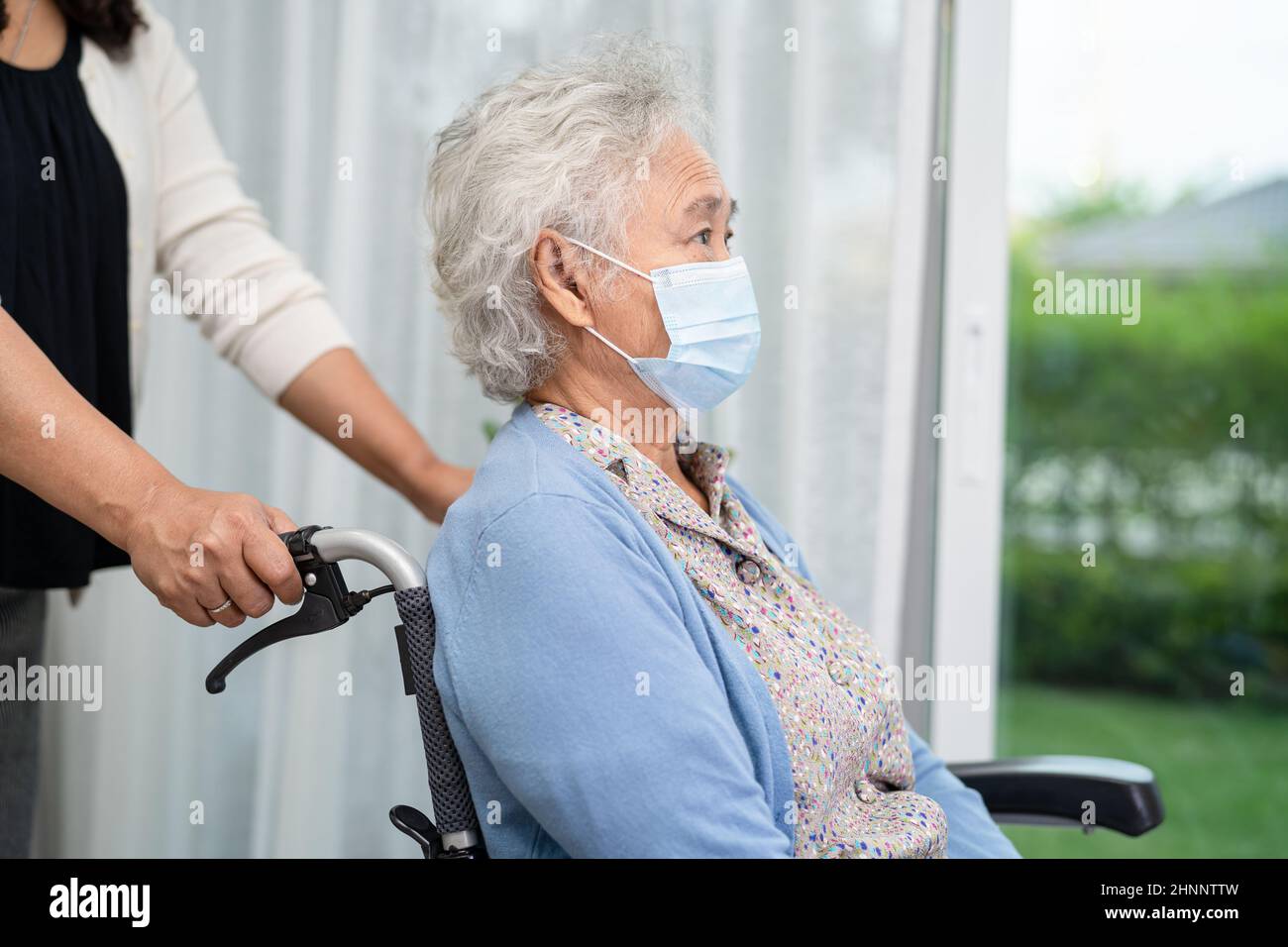 Helfen Sie asiatischen älteren oder älteren Frau im Rollstuhl sitzen und tragen eine Gesichtsmaske zum Schutz der Sicherheitsinfektion Covid-19 Coronavirus. Stockfoto