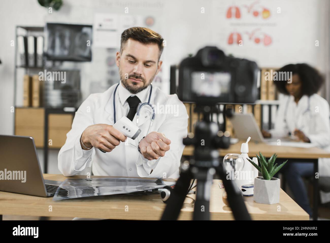 Ein positiver kaukasischer Arzt im Laborkittel hält weiße sterile Handschuhe in den Händen und spricht während der Videoaufzeichnung vor der Kamera. Konzept der Medizin und Social Media. Stockfoto