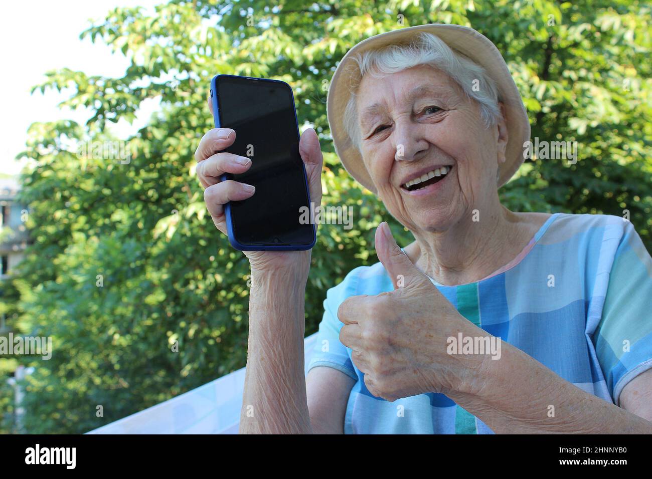 Freudige reife Dame zeigt ein Telefon isoliert auf Natur Hintergrund Stockfoto