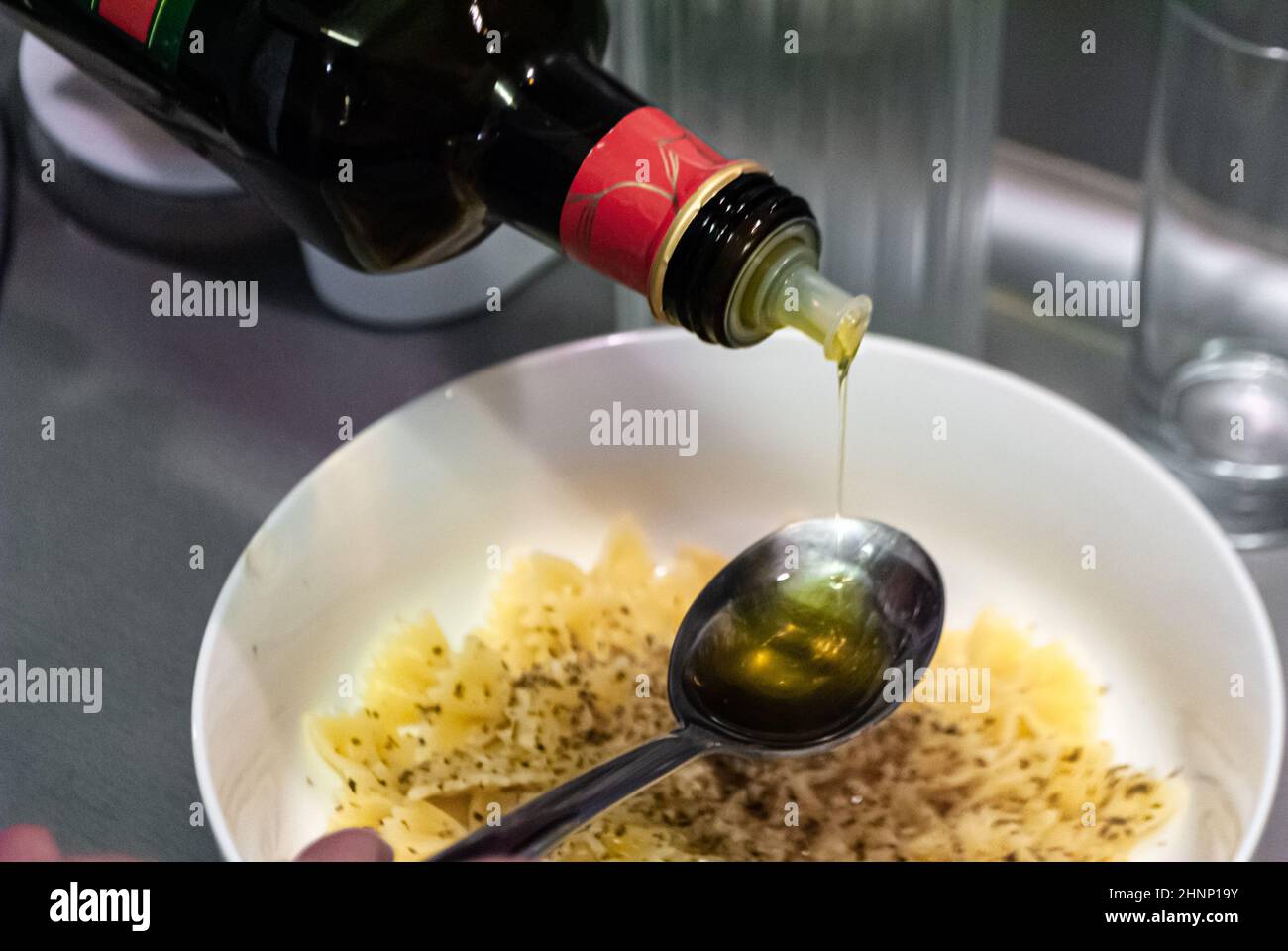 Olivenöl gießt vor dem Hintergrund einer Schüssel mit Pasta in einen Löffel Stockfoto