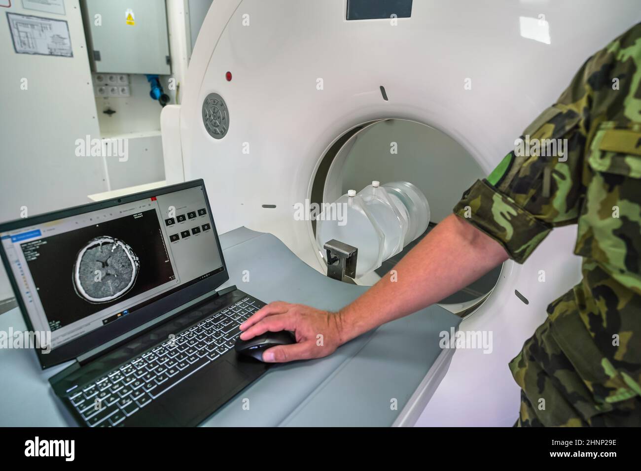 CT- oder Computertomographie-Scanner im mobilen Feldcontainer der Armee, Soldat, der den Patienten mit schweren Kopftrauma-Scans auf dem Laptop in der Nähe zeigt Stockfoto