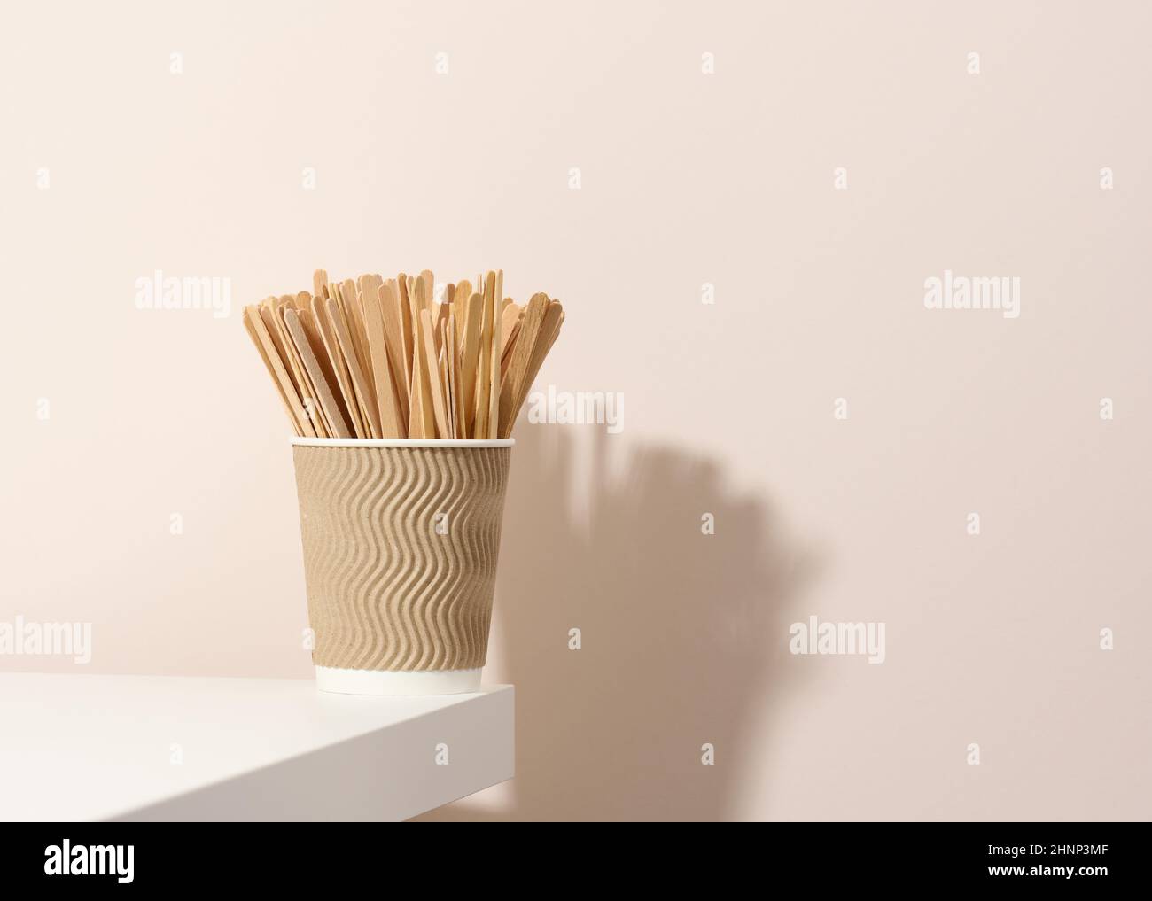 Braune Pappbecher und hölzerne Rührstäbe auf einem weißen Tisch mit beigem Hintergrund. Umweltfreundliches Geschirr, kein Abfall Stockfoto