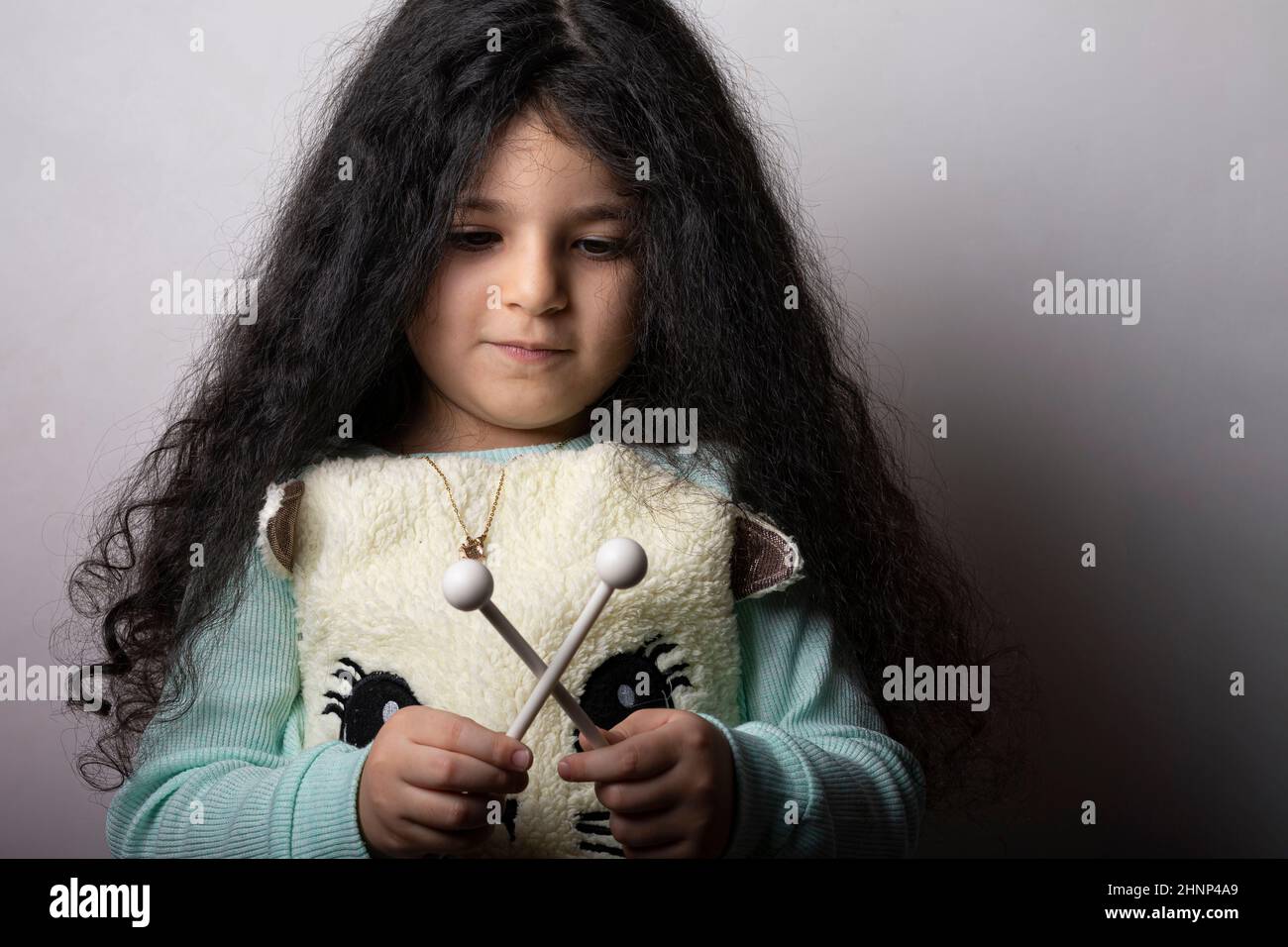 Kleines Mädchenportrait mit Xylophon-Stöcken in der Hand, die nach unten schauen Stockfoto