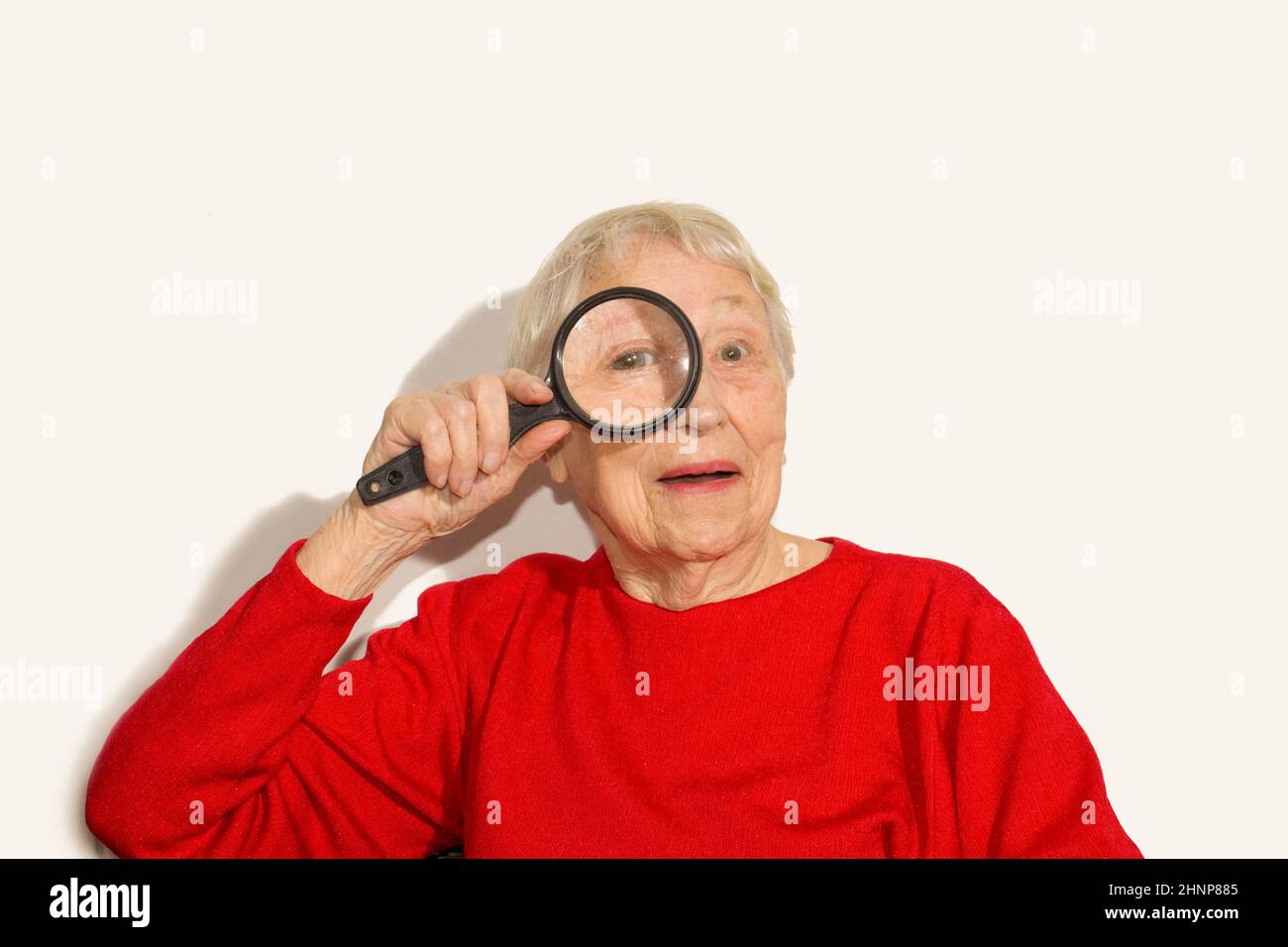 Porträt einer älteren Frau, die durch ein Vergrößerungsglas über Weiß schaut Stockfoto