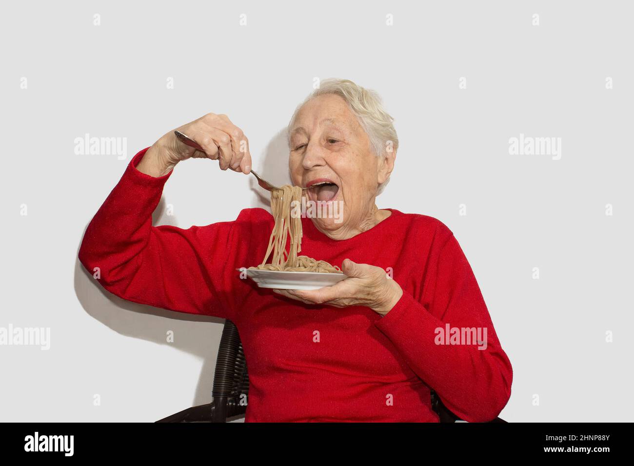 Glückliche ältere Frau, die italienische Spaghetti-Pasta isst, isoliert auf weißem Studio Stockfoto