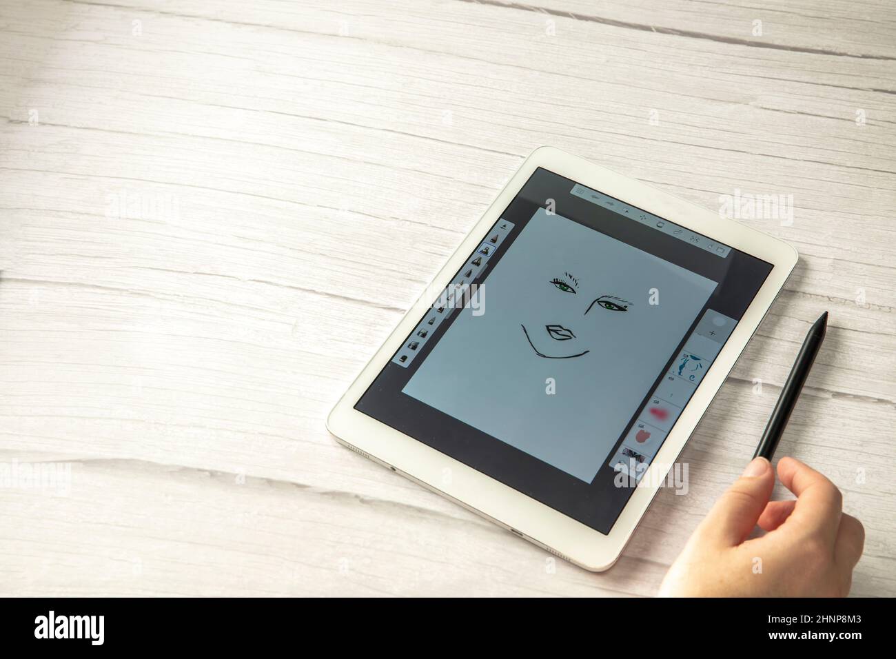 Junger kreativer Designer hält Stylus-Stift Zeichnung auf dem Bildschirm des digitalen Tabletts auf Holzschreibtisch mit Kopierraum, moderne digitale Kunst Draufsicht Stockfoto