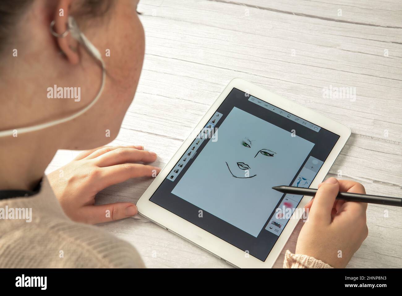 Junger kreativer Designer hält Stylus-Stift Zeichnung auf dem Bildschirm des digitalen Tabletts auf Holzschreibtisch mit Kopierraum, moderne digitale Kunst Draufsicht Stockfoto