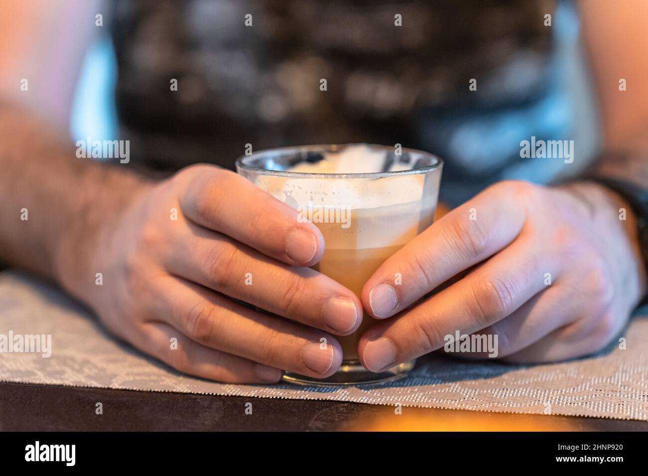 Konzentrieren Sie sich im Vordergrund auf die Hände eines Mannes, der ein Glas Cappuccino hält. Stockfoto