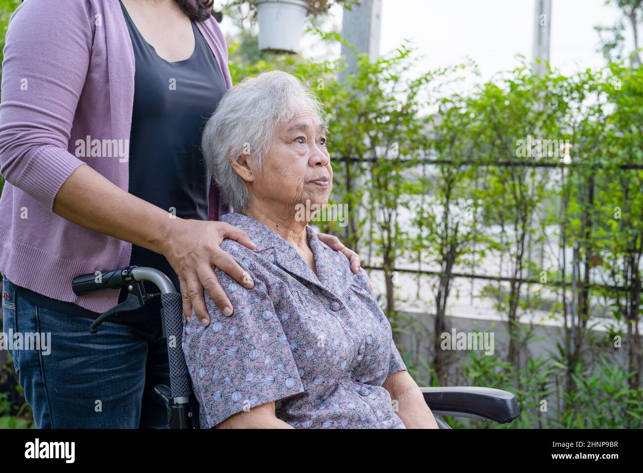 Pflegerin Tochter Hilfe asiatische ältere oder ältere alte Dame Frau auf elektrischen Rollstuhl im Park. Stockfoto