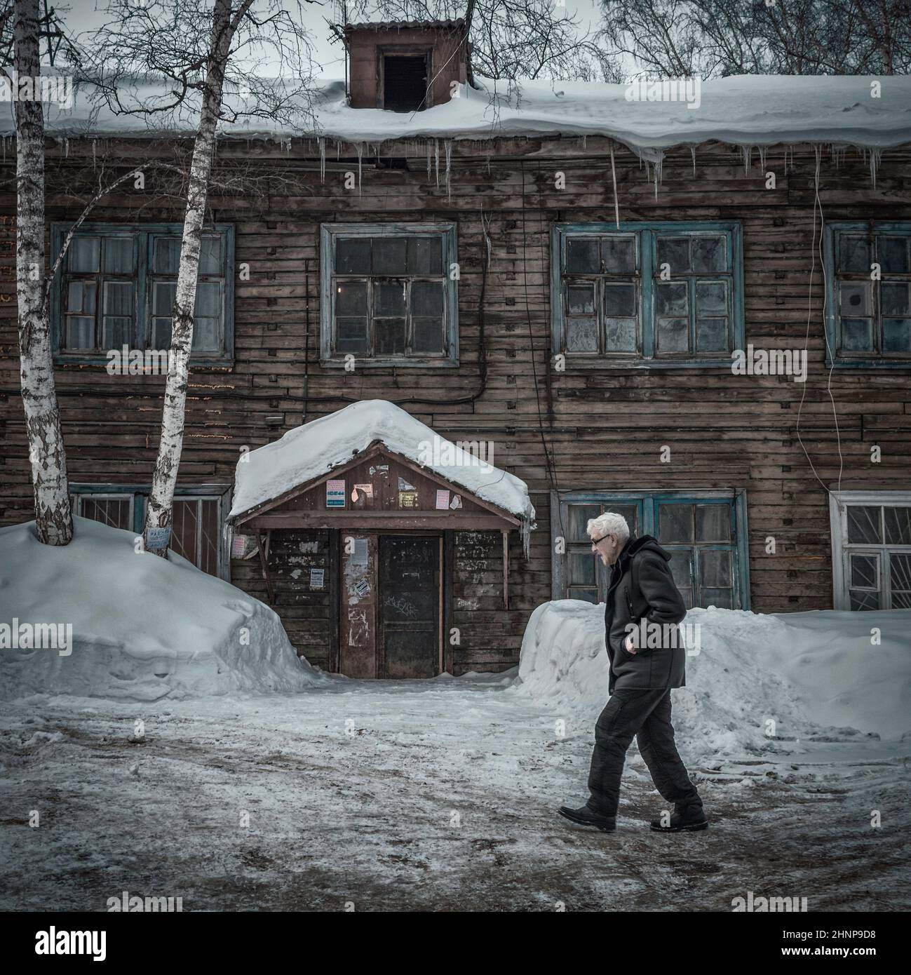 23rd. Februar 2019, Russland, Tomsk, älterer Mann läuft am alten Holzgebäude vorbei Stockfoto