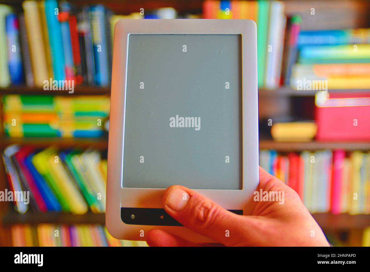 Ebook oder digitale Lesen tablet device. E-Buch in der Hand des Menschen. Im Hintergrund ist das Regal mit hellen echte Bücher. Online shopping Bücher Konzept Stockfoto