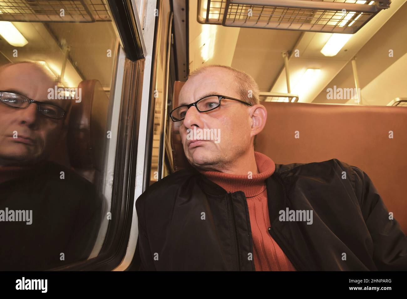 Mittleres alter Mann schaut aus dem Fenster der Bahn. Passagier während der Reise durch hohe Geschwindigkeit Express Zug in Europa. Älterer Mann im Zug in der Nacht unterwegs Stockfoto