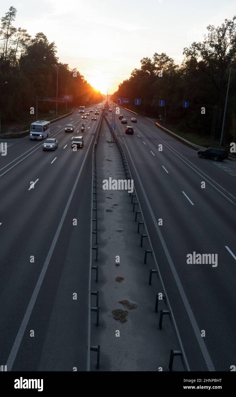 Autos auf der Autobahn bei Sonnenuntergang bewegen. Straßenverkehr bei Sonnenuntergang mit Autos. Viel Verkehr auf der Autobahn, Blick von oben auf die Straße. Stockfoto