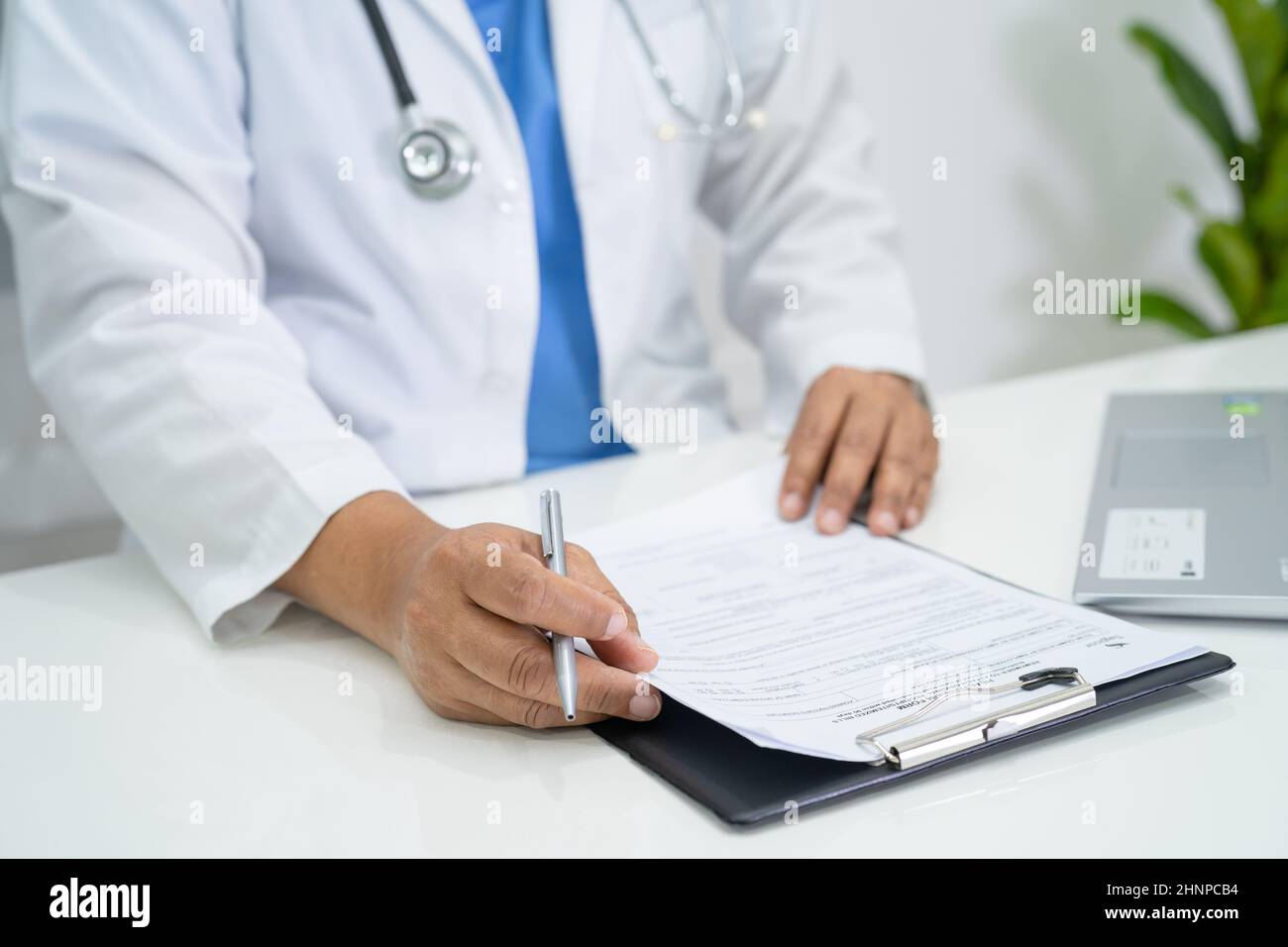 Arzt schreiben Gesundheit medizinische Notiz in Zwischenablage mit Laptop im Krankenhaus. Stockfoto