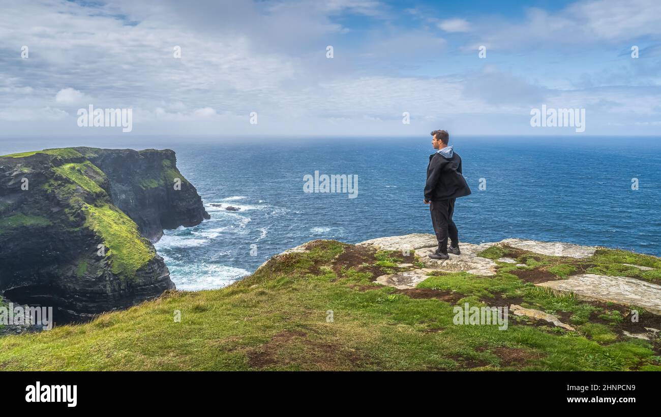 Mann, der auf den berühmten Cliffs of Moher steht und die spektakuläre Aussicht auf Irland bewundert Stockfoto