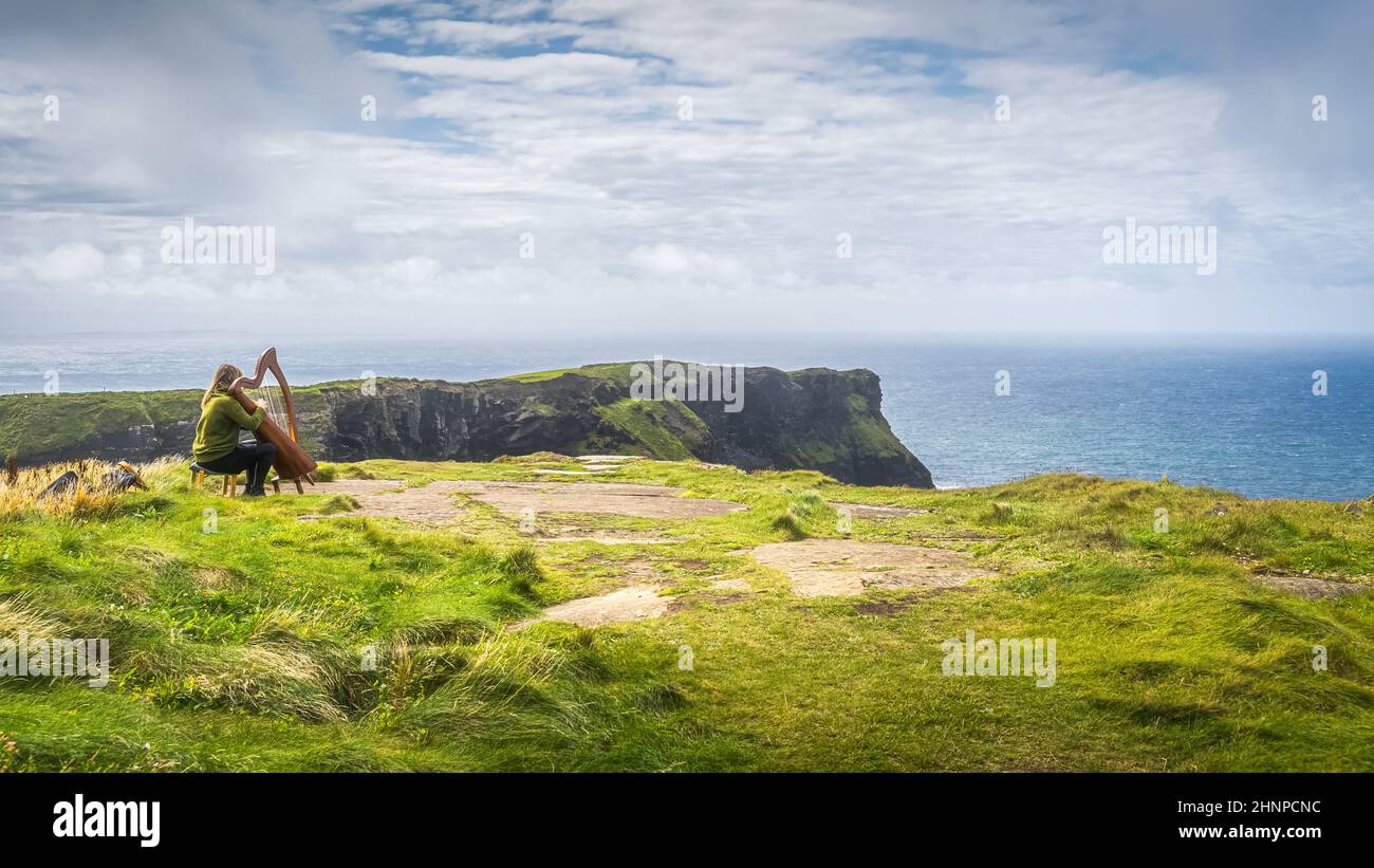 Frau spielt Harfe auf den legendären Cliffs of Moher, Irland Stockfoto