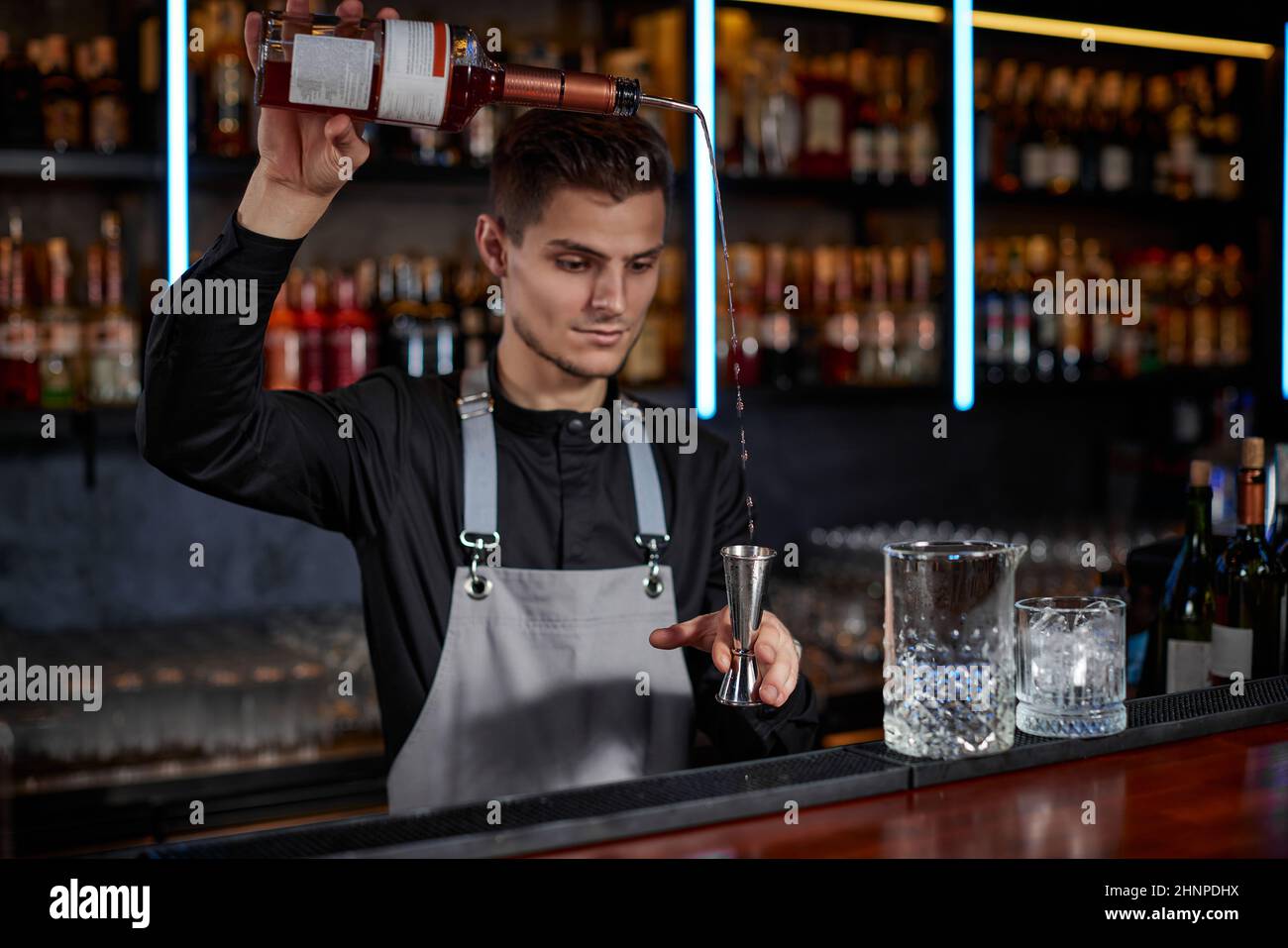 Barkeeper in der Schürze fügt dem Glas Zutaten hinzu Stockfoto