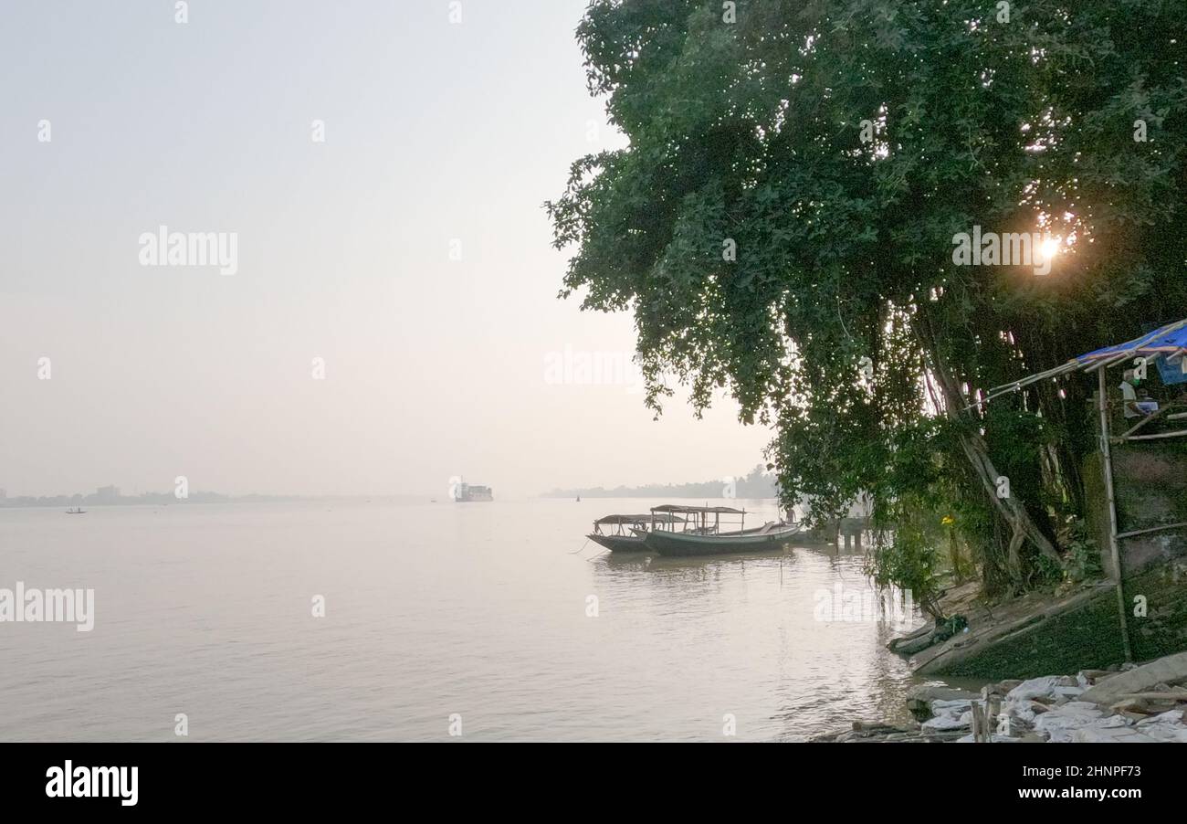 Horizont über dem Fluss gegen klaren Himmel im Hintergrund und Baum im Vordergrund des Flussufers. Blick auf die Landschaft am Ganges-Fluss während des Sonnenuntergangs. Budge Budge Stockfoto