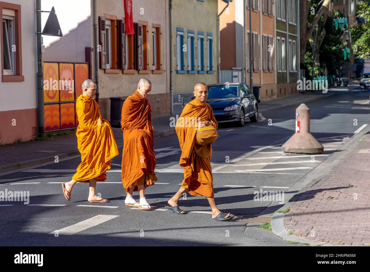 Bettelnde Mönche überqueren morgens in ihrem typischen orangefarbenen Kleid eine Straße mit Körben, um Nahrung zu sammeln Stockfoto