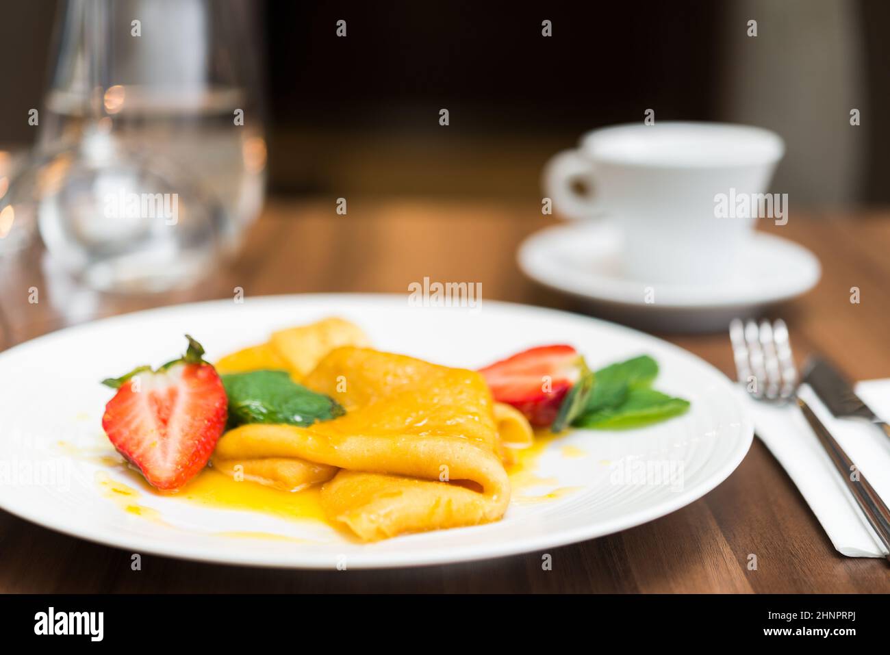 Traditioneller gebratener Pfannkuchen mit Erdbeere und Minze, gekrönt mit Ahornsirup, auf Holztisch und weißem Teller angeordnet. Sehr enge Schärfentiefe. Stockfoto