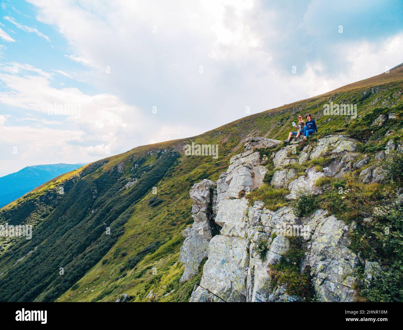 Luftaufnahme des Great Green Ridge. Guy und Girl sitzen auf einem großen Hügel vor dem Hintergrund einer riesigen Berglandschaft Stockfoto
